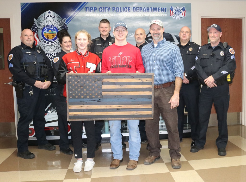 Tipp City Police Department with two students gifting them a flag.