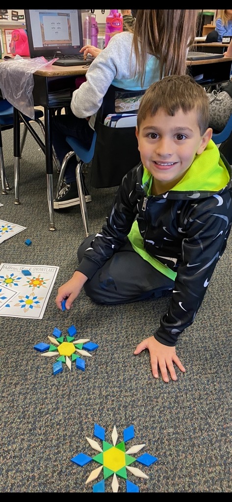 A first grade boy shows off his snowflake made with blocks.
