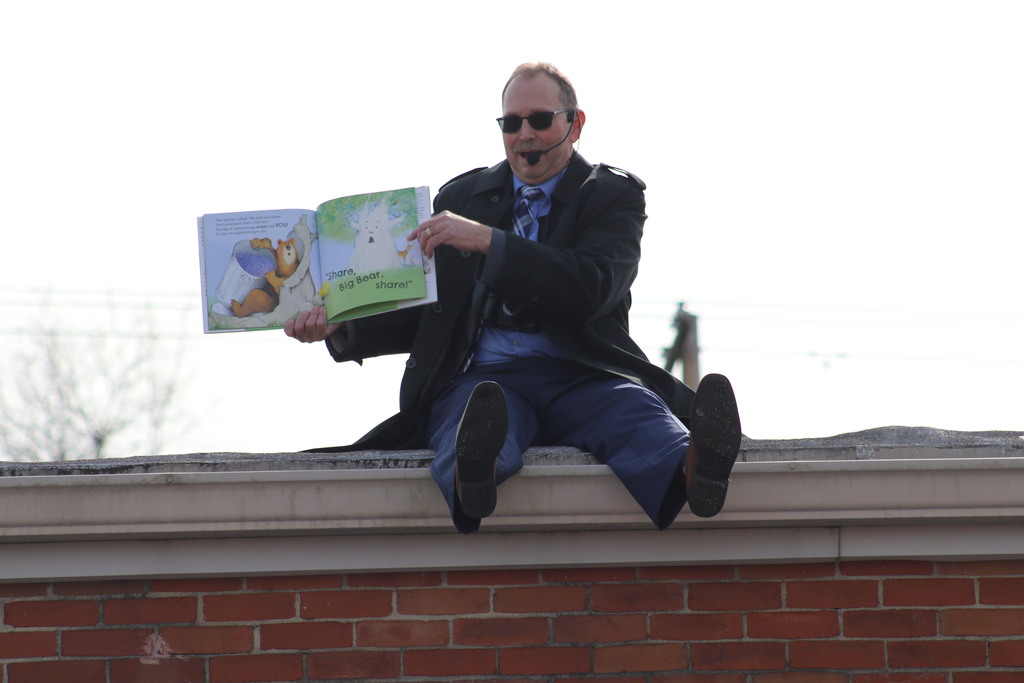 Mr. G flipping the page of a book while on the roof reading to kids on the playground.