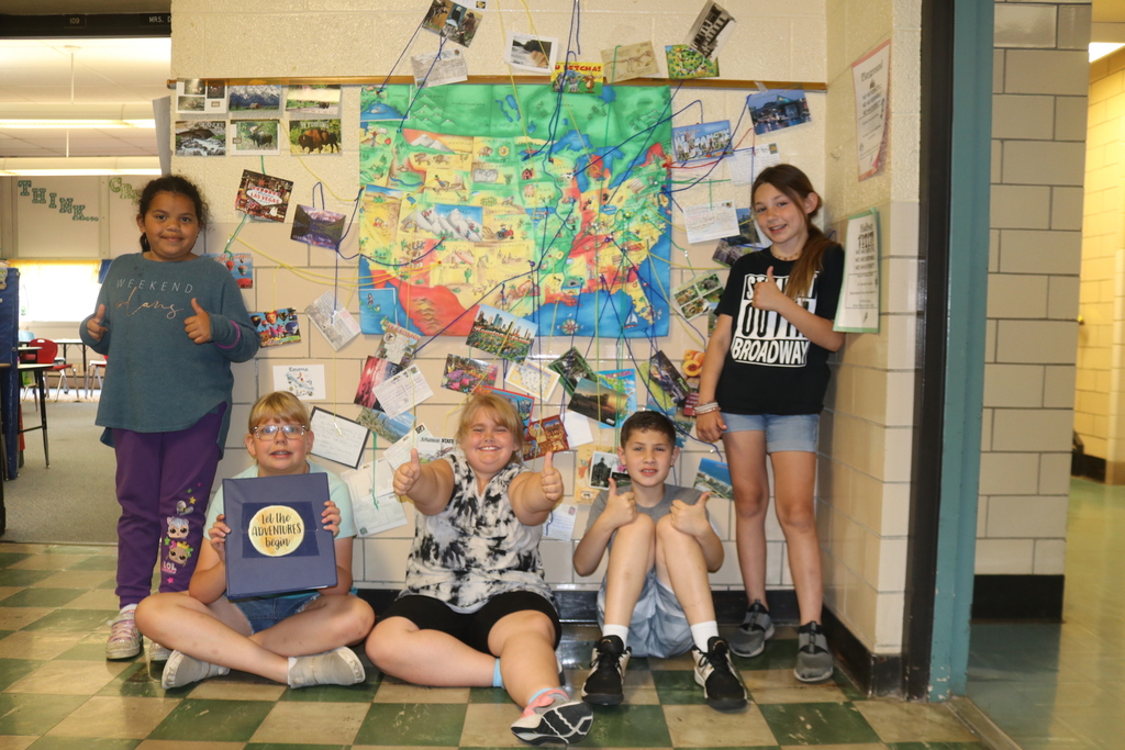 Students pose in front of the map with postcards.