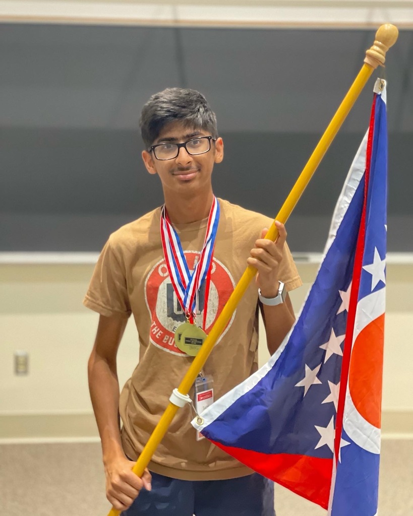 Sadhil Mehta holding a flag and wearing two medals.