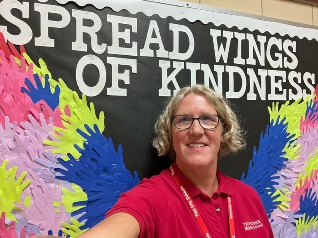 Mrs. Fetters takes  selfie in front of the kindness bulletin board.